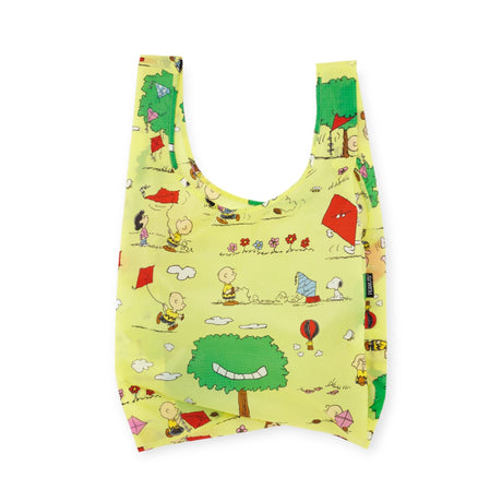 This eco-friendly Baggu Standard - Peanuts Kite Eating Tree reusable bag is a delightful creation featuring yellow-themed cartoon characters flying kites, playing in a park, and surrounded by trees, flowers, and balloons.