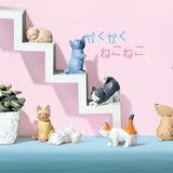 The Geometric Cats Blind Box by Yell, a delight for cat lovers, is showcased on a staircase shelf surrounded by plants, with Japanese text elegantly adorning the background.