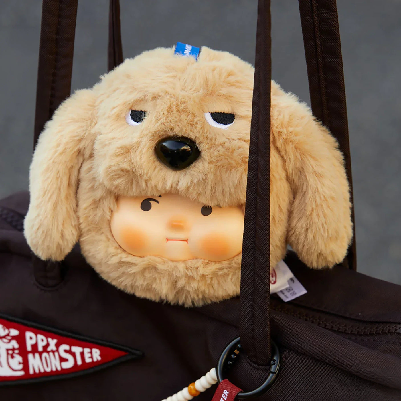 Plush dog keychain with tan fur, dark eyes, black nose, hanging strap on bag