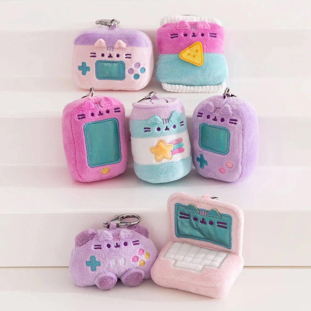 Seven plush keychains from the Pusheen Blind Box - Gamer Series by Pusheen, featuring retro tech gadgets and cats like a laptop, game controller, and digital pet, are displayed on white steps.