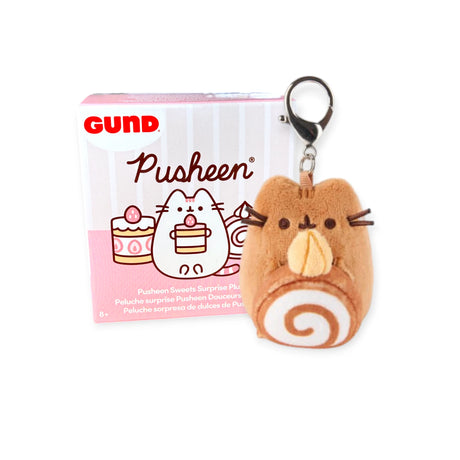 A cinnamon roll-shaped Pusheen plush keychain from the Pusheen Blind Box - Sweets Series sits beside its pink and white packaging, a delightful treat for fans of the Pusheen brand.