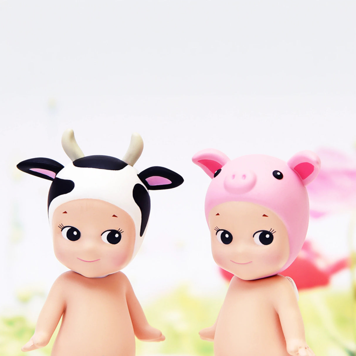 Two figurines from the Sonny Angel Animal Version 2 Series by Sonny Angel, each featuring a human-like body with one wearing a cow-themed hat and the other a pig-themed hat, are set against a softly blurred background. These delightful figures are part of the charming Animal Series V2 Blind Box selection and add an adorable touch to any display.