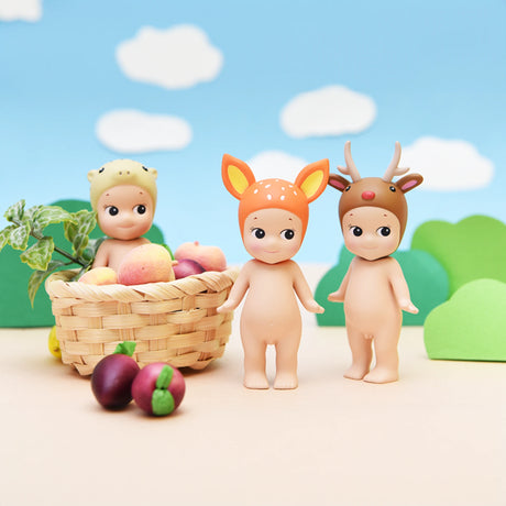 Three figures from the Sonny Angel Animal Version 2 Series by Sonny Angel are displayed near a basket of fruits, each wearing an adorable animal-themed hat. It's like revealing a delightful surprise from a blind box, with each character contributing its own whimsical flair to the scene.