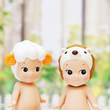 Two Sonny Angel figurines from the Sonny Angel Animal Version 2 Series stand side by side, each emerging from a blind box. One is adorned with a sheep hat featuring yellow horns, and the other wears a hedgehog hat. Both display cheerful smiles against a softly blurred background.