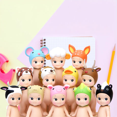 A delightful arrangement of twelve dolls from the Sonny Angel Animal Version 2 Series showcases their charming hats. Complementing the scene are a notebook, pencil, and tape dispenser in the background, reminiscent of a delightful blind box discovery.