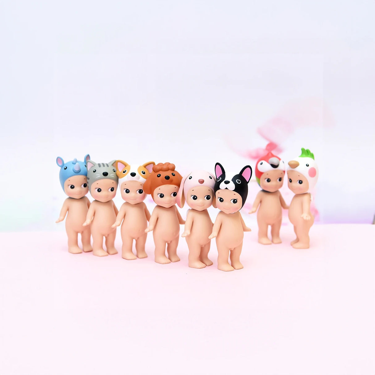 A row of figures from the Sonny Angel Animal Version 3 Series by Sonny Angel stands on a light surface with a soft-focus background. Each one is adorned with colorful animal hats, making these blind box collectibles a charming addition to any collection.