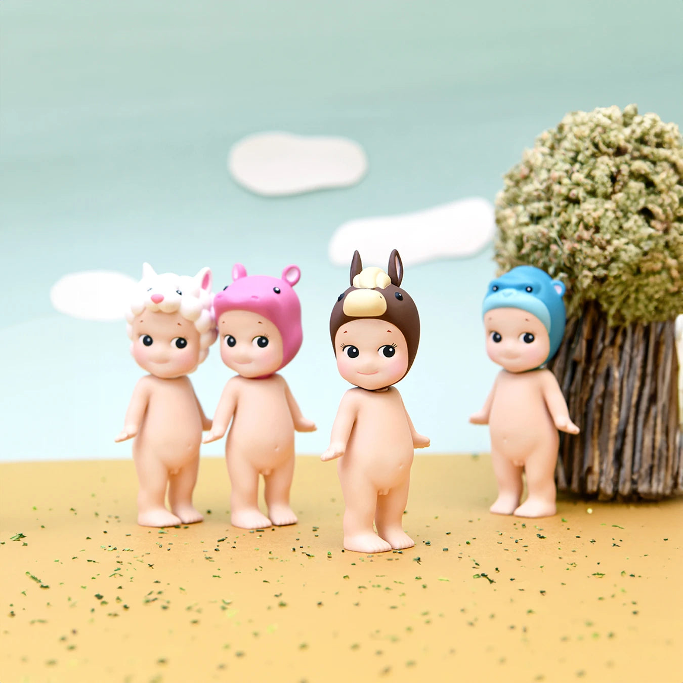 Four charming figures from the Sonny Angel Animal Version 4 Series, each donning unique animal-themed hats, stand on a sandy surface with a tree and sky in the background. These collectible dolls from the Sonny Angel brand bring a delightful sense of whimsy, capturing the excitement of being unearthed from their blind box beginnings.