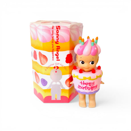 Birthday cake mini figurine in pink frosting dress, standing beside gift box