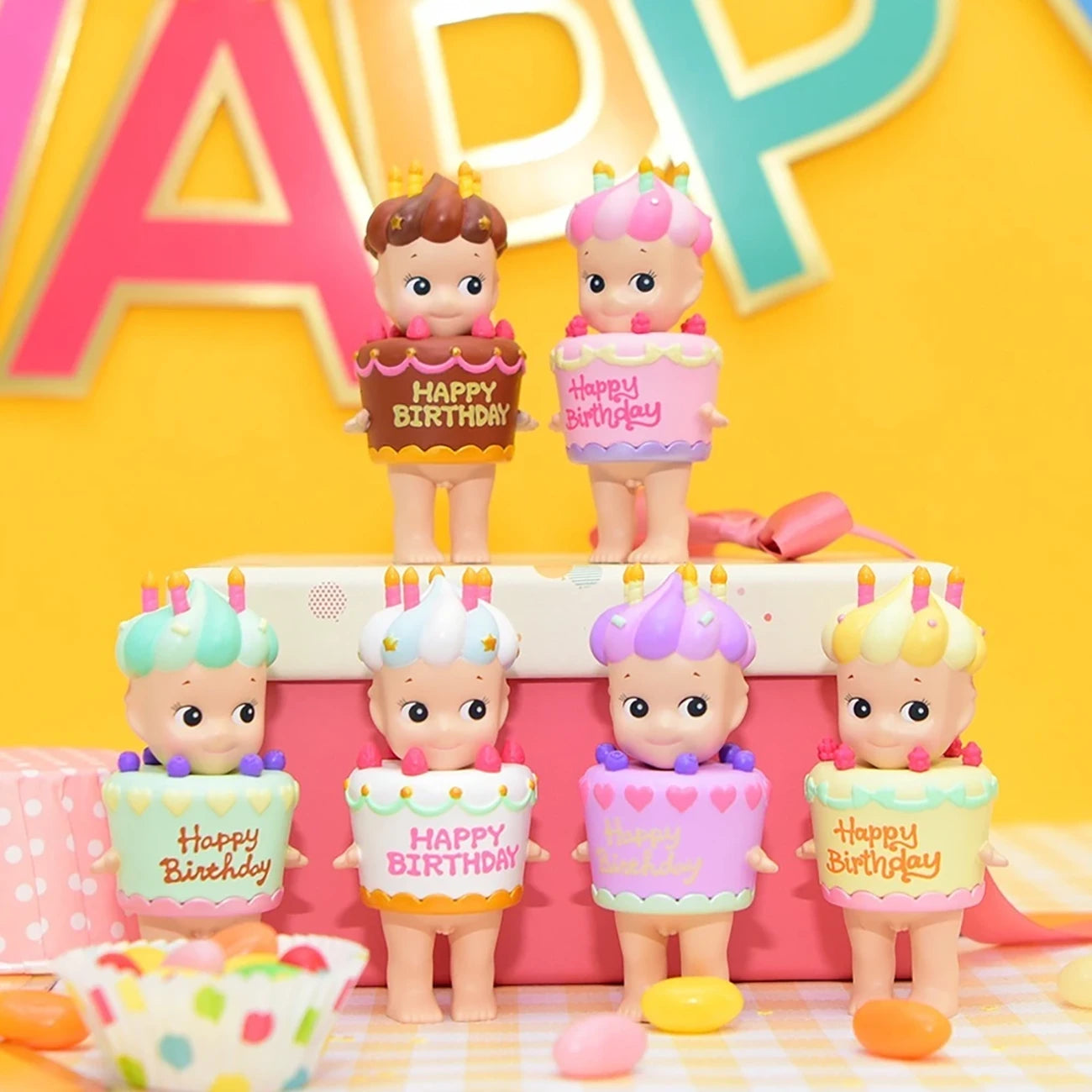 The charming Sonny Angel Happy Birthday Cake Gift figurines by Sonny Angel, each dressed in a delightful cake-themed outfit complete with "Happy Birthday" lettering, are artfully displayed amidst colorful birthday decor, providing an exciting surprise similar to a Blind Box experience.