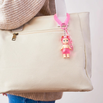 Pink doll keychain charm hanging from a beige tote bag
