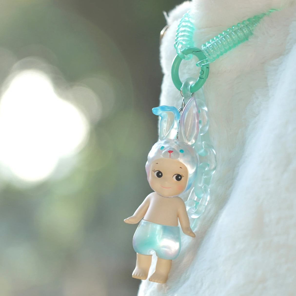 A charming Sonny Angel Candy Store Series doll, wearing bunny ears and blue shorts, is attached to a blue keychain, hanging against a fluffy white backdrop.