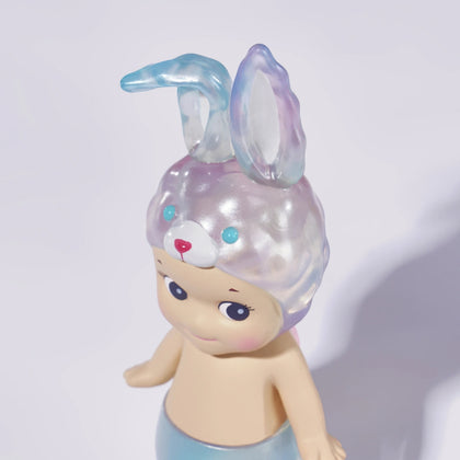 A Sonny Angel Candy Store Series plastic figurine, with a rabbit-eared hat and mermaid tail, stands against a plain background, capturing the brand's whimsical charm.