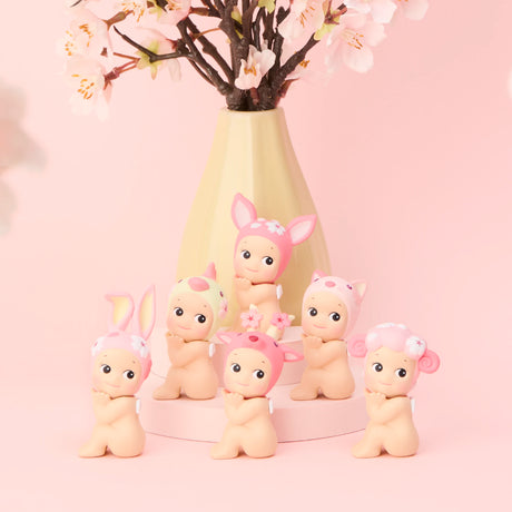 Six charming Sonny Angel Cherry Blossom Series figurines, each wearing unique animal ear hats and flower accents, are displayed before a vase of pink cherry blossoms on a pastel background. This limited edition from Sonny Angel is ideal for collectors seeking something unique and adorable.