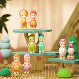 A set of six vibrant Sonny Angel toy figures from the limited edition Dinosaur Series, each wearing an animal hat, are displayed on tiered wooden platforms. The scene is enhanced by decorative trees and spheres in the background, adding a whimsical charm to these prehistoric companions.