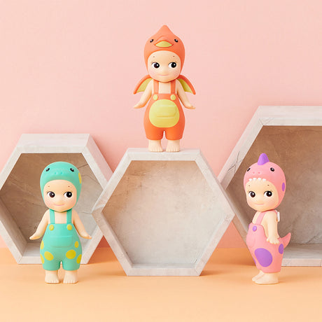 Three figures from the Sonny Angel Dinosaur Series by Sonny Angel are playfully arranged on and around hexagonal shelves, set against a pink backdrop, creating a whimsical scene with these prehistoric pals.