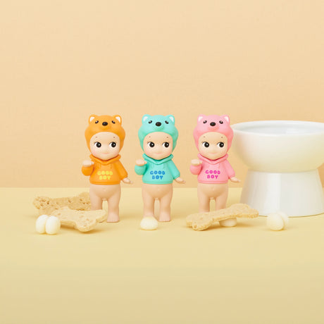 Three figures from the Sonny Angel Dog Time Series by Sonny Angel, each featuring animal-themed hats, are arranged in a row. These collectible mystery figures are set against a beige background, adorned with bone-shaped biscuits and small white balls.