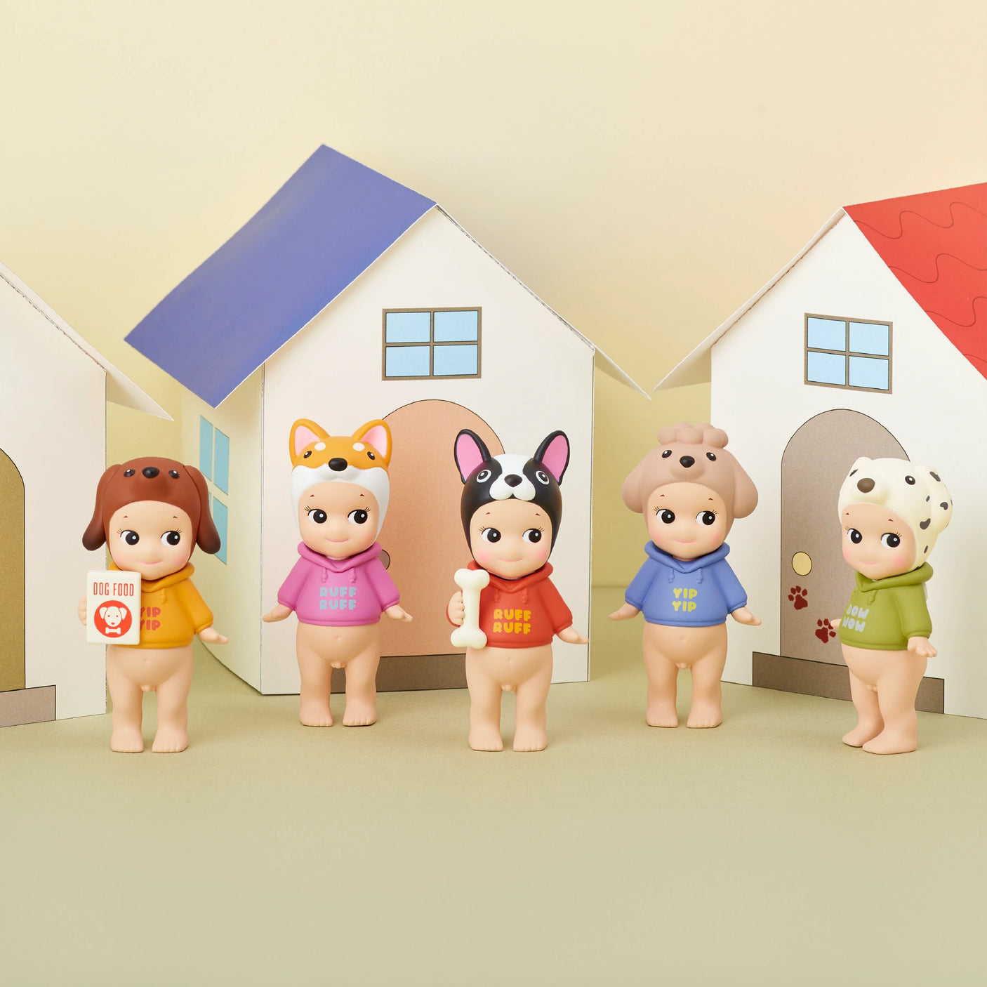 Five collectible figures from the Sonny Angel Dog Time Series by Sonny Angel, each dressed in animal-themed hats and vibrant shirts, stand before paper houses with various accessories in hand. These mystery figures charmingly represent different dog breeds in miniature form.