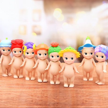 A collection of small toy figurines with vibrant, colorful headpieces stands on a wooden surface. Each from the Sonny Angel Flower Series by Sonny Angel showcases unique plant or flower-themed headwear. Uncover the allure of these floral figures as they bring whimsy to your collection—each a delightful surprise from a blind box.