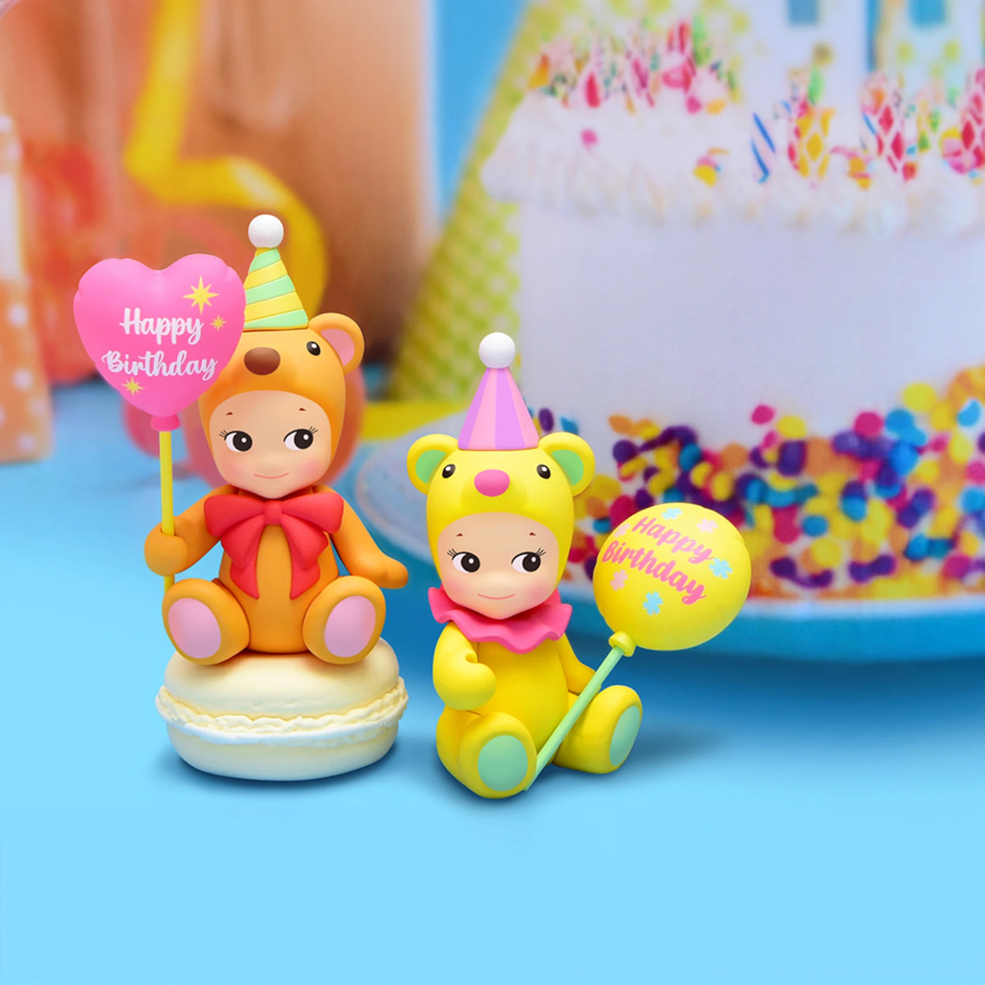 Two Sonny Angel Birthday Bear Gift figurines, wearing festive party hats and holding celebratory signs, are perched on a macaron with a vibrant birthday cake shining brightly in the background—a delightful gift to charm any celebration.