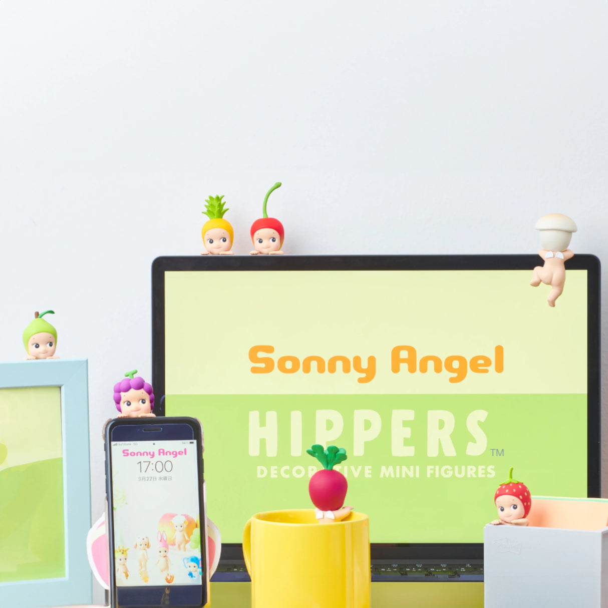 Sonny Angel Hippers Blind Box - Harvest figures from the Sonny Angel brand beautifully decorate a desk, accompanied by a laptop showcasing "Sonny Angel Hippers." Each delightful figure sits on a phone, mug, and monitor, wearing playful fruit or vegetable headgear.