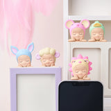 Five figurines from the Sonny Angel Hippers Blind Box - Dreaming collection, each donning unique animal hats, sit charmingly on a white and purple shelf beside a smartphone.