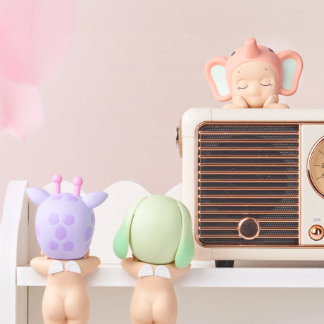 Three Sonny Angel Hippers from the Dreaming collection, each sporting animal-themed hats, are arranged on a white shelf. Two gaze upward while one, identified as a Secret Unicorn, is perched atop a vintage radio.