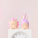 Two figures wearing animal-themed hats, featuring a pink lion and a purple bunny, peacefully rest atop a white clock showing 12:00. As part of the Sonny Angel Hippers Blind Box - Dreaming collection by Sonny Angel, these enchanting characters embody whimsy and charm in every detail.