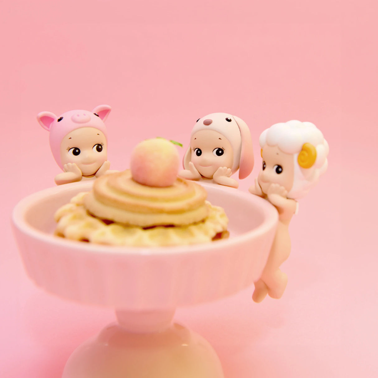 Three charming Sonny Angel Hippers Blind Box figurines from the Sonny Angel Animal Series are arranged around a pink cake stand adorned with pancakes topped with a peach, set against a soft pink background.