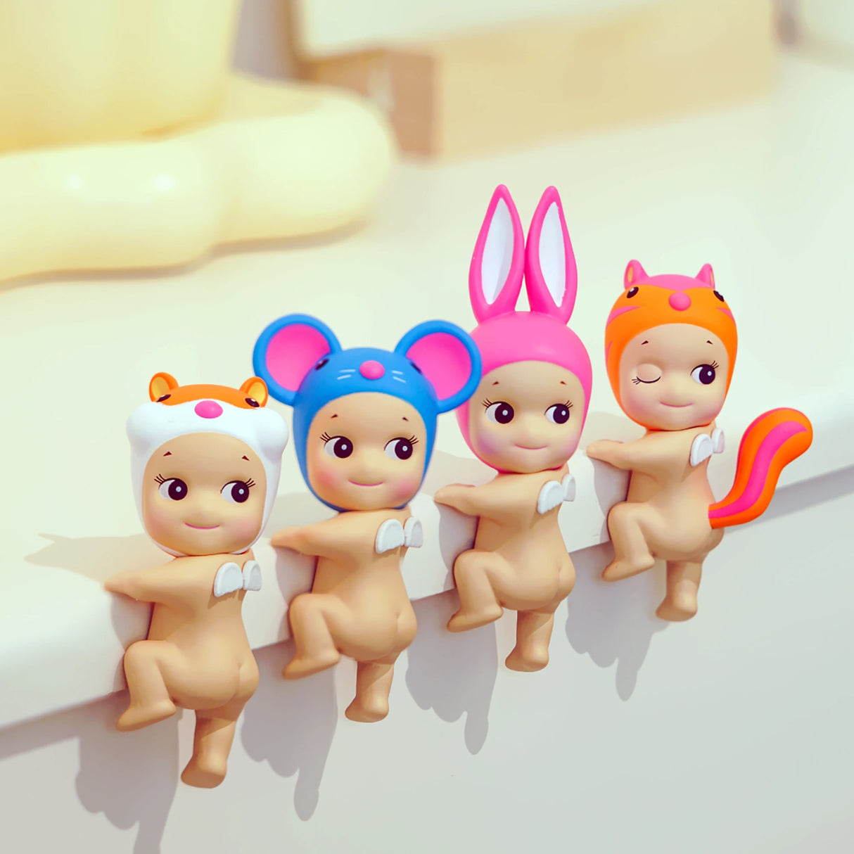 Four Sonny Angel Hippers Blind Box figures sporting hats inspired by the Looking Back series sit on an edge, featuring designs that resemble a bear, mouse, rabbit, and squirrel.