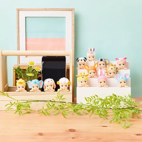 A set of Sonny Angel Hippers Blind Box - Animals by Sonny Angel, featuring adorable baby figurines wearing animal-themed hats, displayed on a wooden surface. These delightful items come with a reusable adhesive base, allowing you to reposition them easily for dynamic and ever-changing displays.