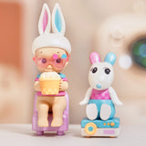 A doll with bunny ears and pink glasses, holding a popcorn cup, sits beside a cartoonish white rabbit figure on a colorful stand, bringing to mind the cozy companions of the Sonny Angel Home Sweet Home Series by Sonny Angel.