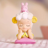 This charming figurine from the Sonny Angel Home Sweet Home Series by Sonny Angel features a sheep with yellow horns and closed eyes, comfortably resting on a pink pillow. It is accompanied by a small pink rabbit cheekily perched on its head.