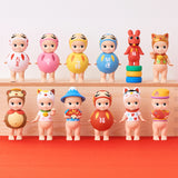 A set of 12 vibrant, small Sonny Angel Japanese Good Luck figures from the Sonny Angel brand, each featuring unique outfits and poses, elegantly arranged on a wooden platform reminiscent of Japanese Lucky Charms, set against a simple backdrop.