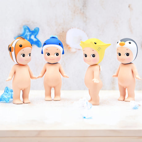 Four Sonny Angel figurines from the Marine Series stand on a light surface, each adorned with a whimsical hat resembling animals such as a clownfish, seal, ray, and penguin. This collection is truly a collector's dream from the brand Sonny Angel, providing the excitement of discovering a charming mystery figure.