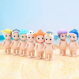 Eight toy figurines from the Sonny Angel Marine Series, each wearing distinctive animal-themed hats, are displayed on a sandy surface. It's a dream come true for collectors.