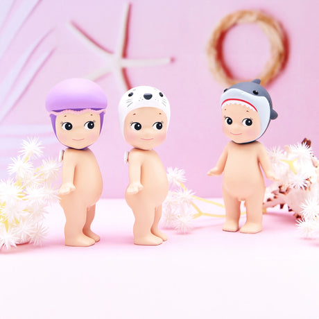 Three adorable figurines from the Sonny Angel Marine Series, each wearing an animal-themed helmet, are displayed on a pastel background adorned with starfish and floral decorations, making them a dream for every collector.