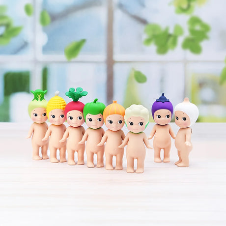 Seven small figurines from the Sonny Angel Vegetable Series Blind Box, each with a unique vegetable-themed hat, stand in a row on a white surface against a blurred window background.