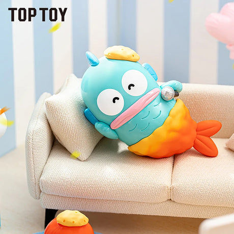 Turquoise cartoon fish character with big eyes, pink lips, and orange tail lounging on beige sofa with pillow.