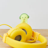 On a wooden surface, yellow headphones are adorned with a charming Smiski Hippers figure donning its own miniature headphones. This delightful addition is from the Smiski Hippers Blind Box collection, adding an element of surprise to your tech setup.