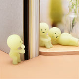 Three small, yellow, glow-in-the-dark plastic figurines from Smiski Series 1—featuring humanoid shapes where one holds a book, another sits, and the third reclines on a wooden surface—evoke curiosity much like treasures revealed from their blind box.