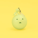 Yellow-green Smiski keychain figure on a round charm with metal clasp