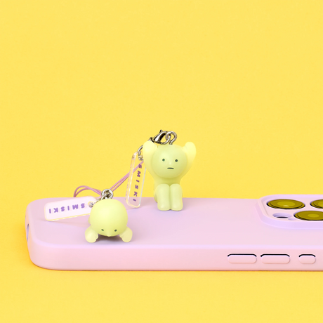 Two small pale yellow character keychains with expressions attached to lavender phone on yellow background