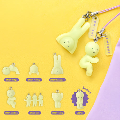 Two pale yellow flexible character keychains with simple faces on purple straps against yellow and lilac background