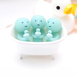 Three round-headed figures from the Smiski Bath Series by Smiski sit together in a white bathtub, each holding small duck toys. These blue collectible figures have a glow-in-the-dark effect, and a larger rubber duck is visible in the background.