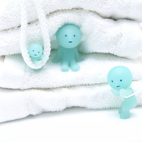 Three Smiski Bath Series figurines, from the Smiski brand's blind box collection, are posed among folded white towels, adding a whimsical touch with their subtle glow-in-the-dark charm.