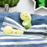 On a blue and white striped cloth, two small figurines from the Smiski Bed Series - Blind Box rest gently. One appears to be asleep, while the other is holding a tiny object. A plant and a green star in the background create a tranquil atmosphere for these charming bedtime buddies by Smiski.