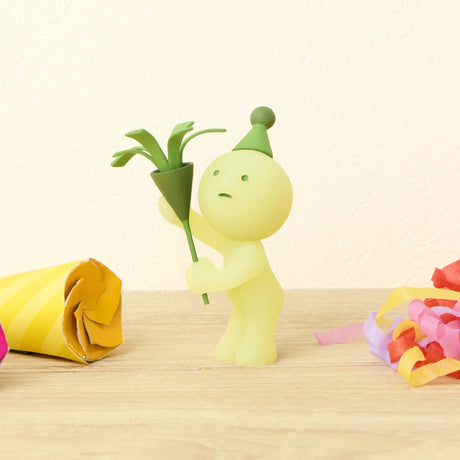 The Smiski Birthday Series - Blind Box by Smiski features a small, round figurine in a green party hat holding a green party popper, surrounded by colorful streamers. This collectible glows in the dark and is available as a blind box.