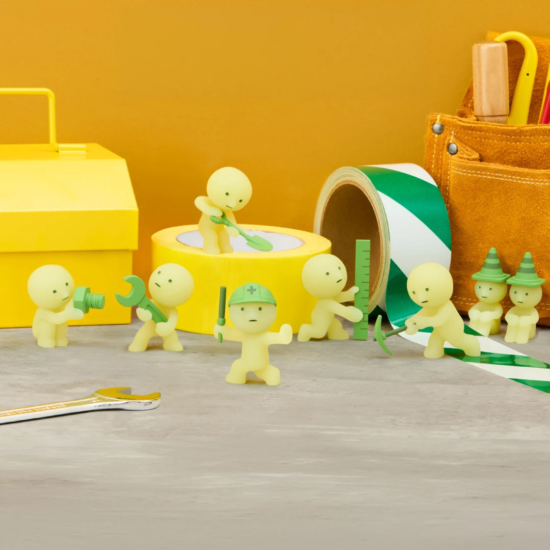 Smiski construction figure holding tools, light green, standing next to yellow storage box