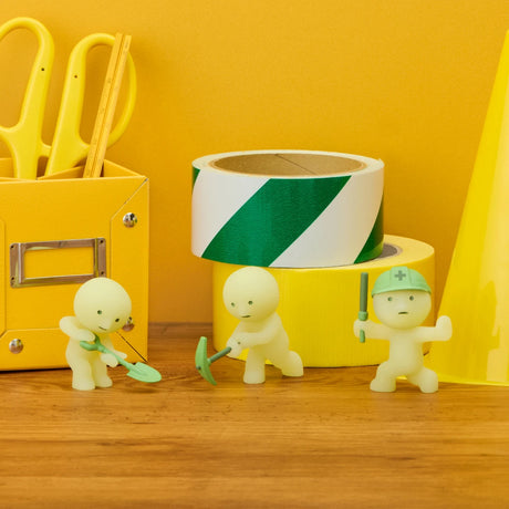 Three construction figures beside a rolled green-and-white tape and a yellow toolbox