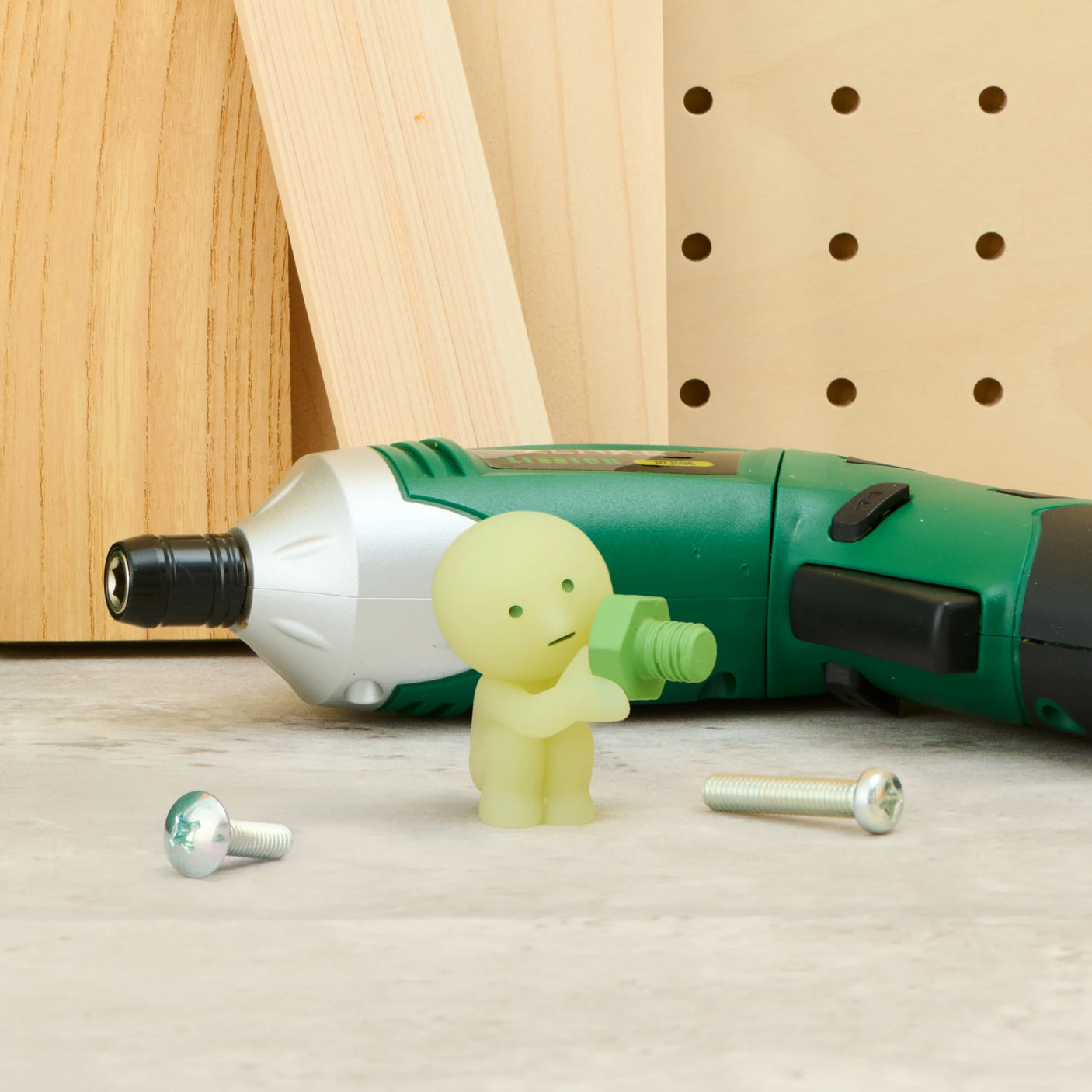 Smiski construction figure beside green drill toy, light green mini figure on white floor